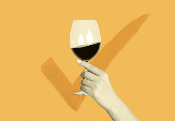 Hand holding up a wine glass with a large checkmark behind it.